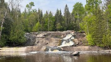A natural landscape with a waterfall, rocky terrain, and dense forest.