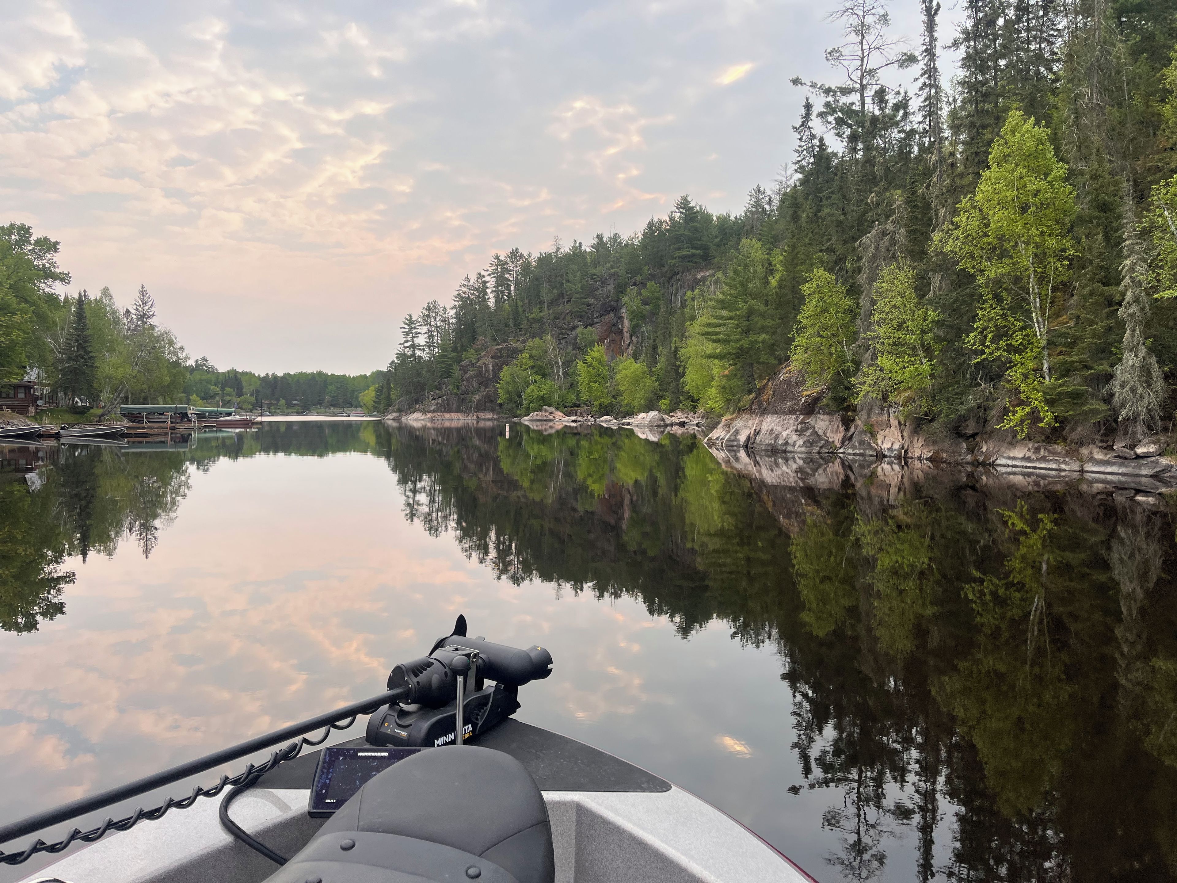 A calm lake with reflections of trees and a dock with boats.