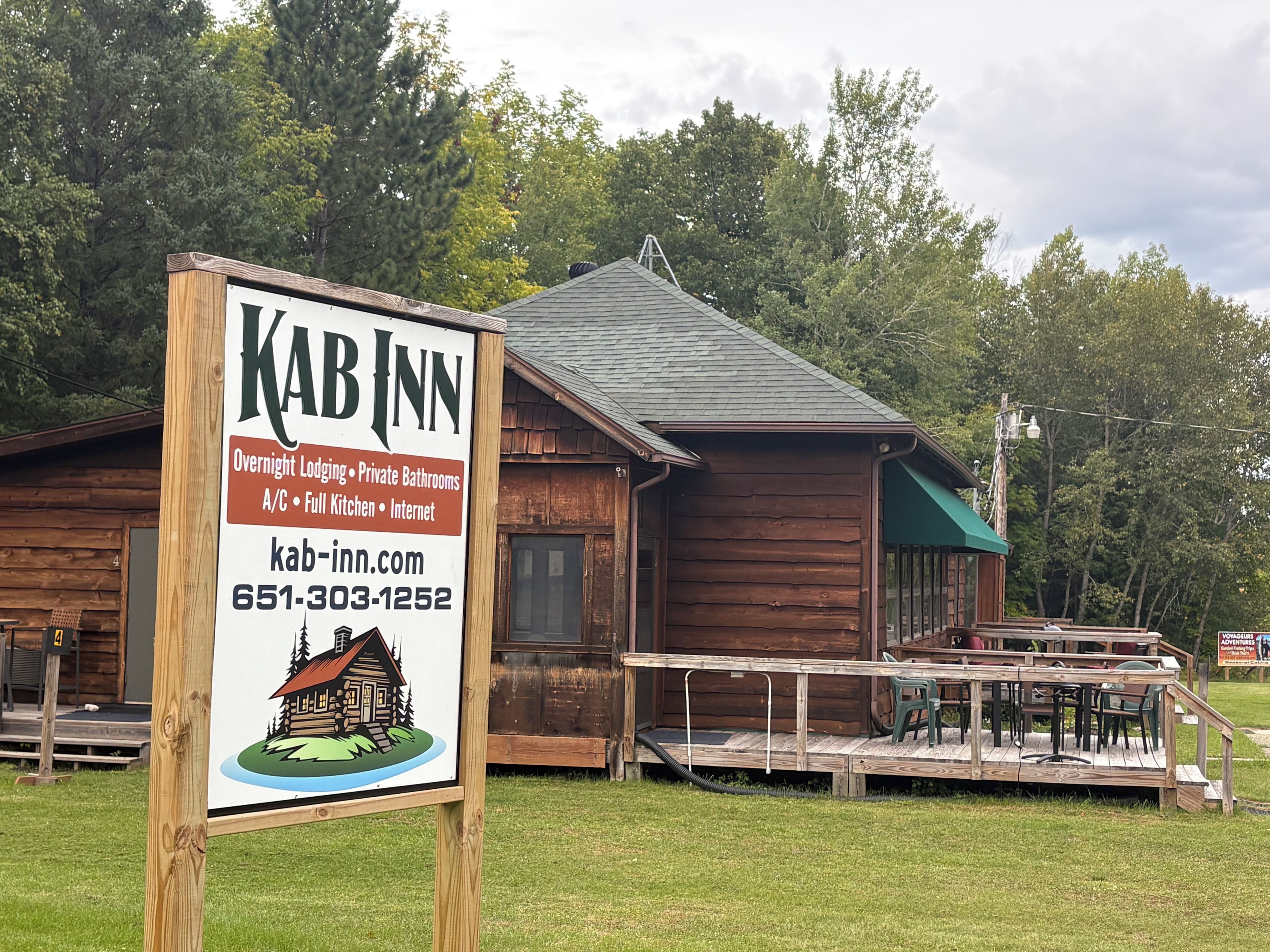 A wooden cabin-style building with a signboard advertising overnight lodging, private bathrooms, full kitchen, and internet.