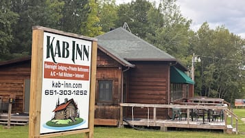 A wooden cabin-style building with a signboard advertising overnight lodging, private bathrooms, full kitchen, and internet.