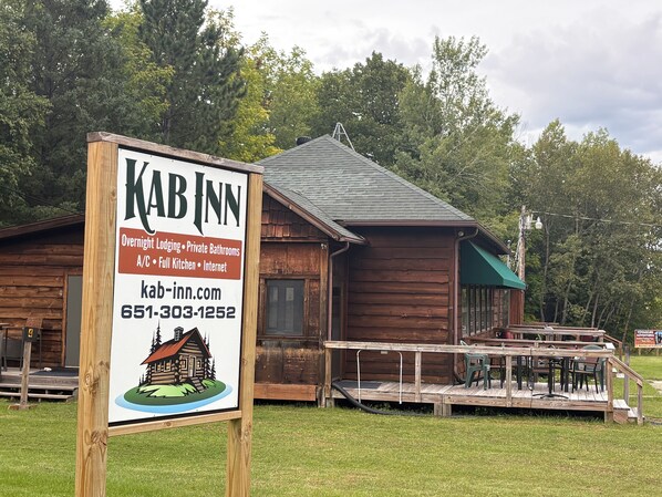 A wooden cabin-style building with a signboard advertising overnight lodging, private bathrooms, full kitchen, and internet.