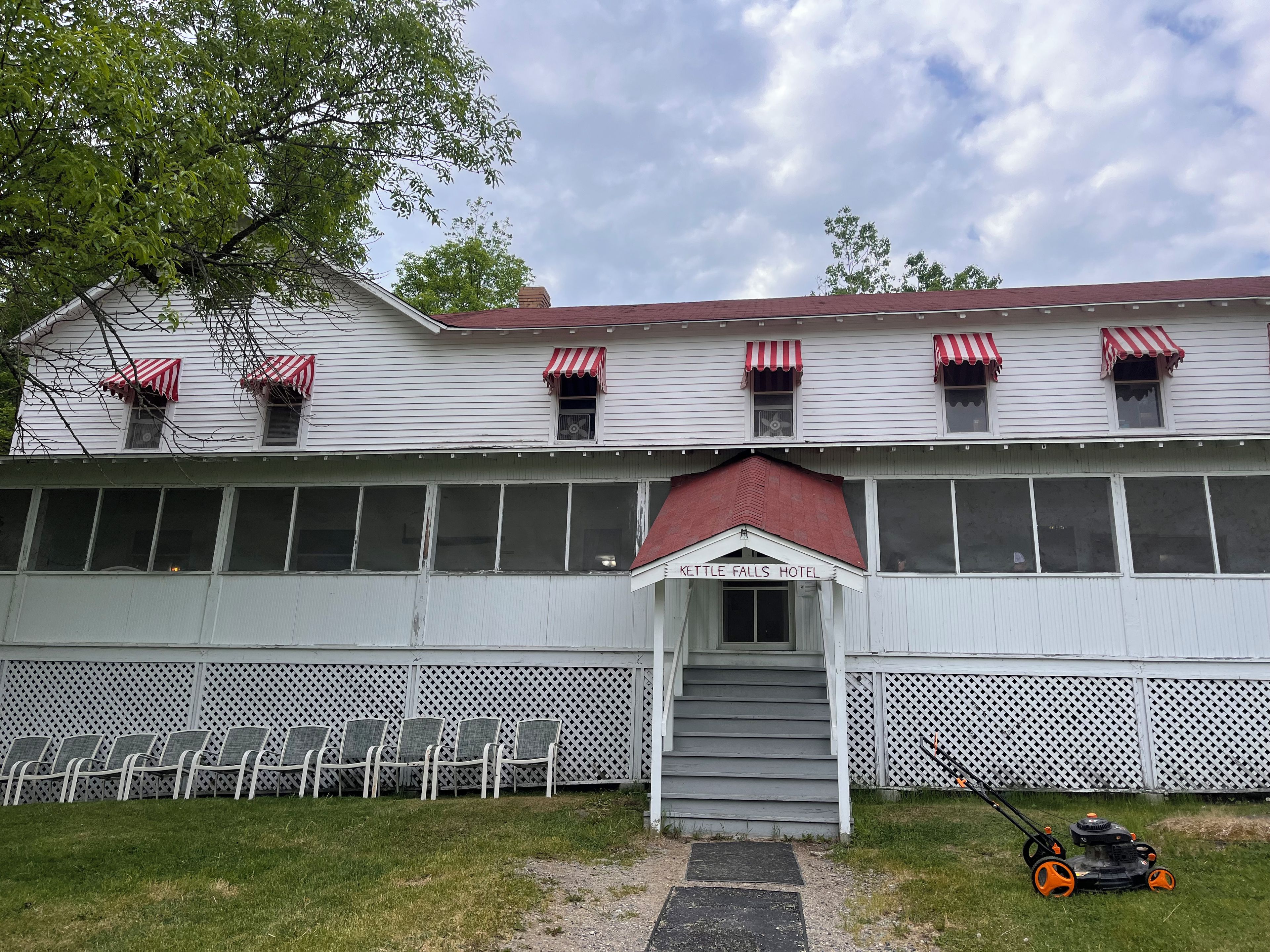 A hotel with a red awning, a staircase leading to the entrance, and a row of chairs outside.
