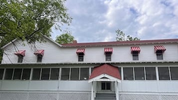 A hotel with a red awning, a staircase leading to the entrance, and a row of chairs outside.
