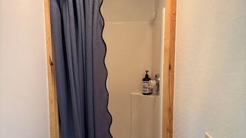 A shower with a blue curtain, a soap dispenser, and a wooden frame around the shower area.