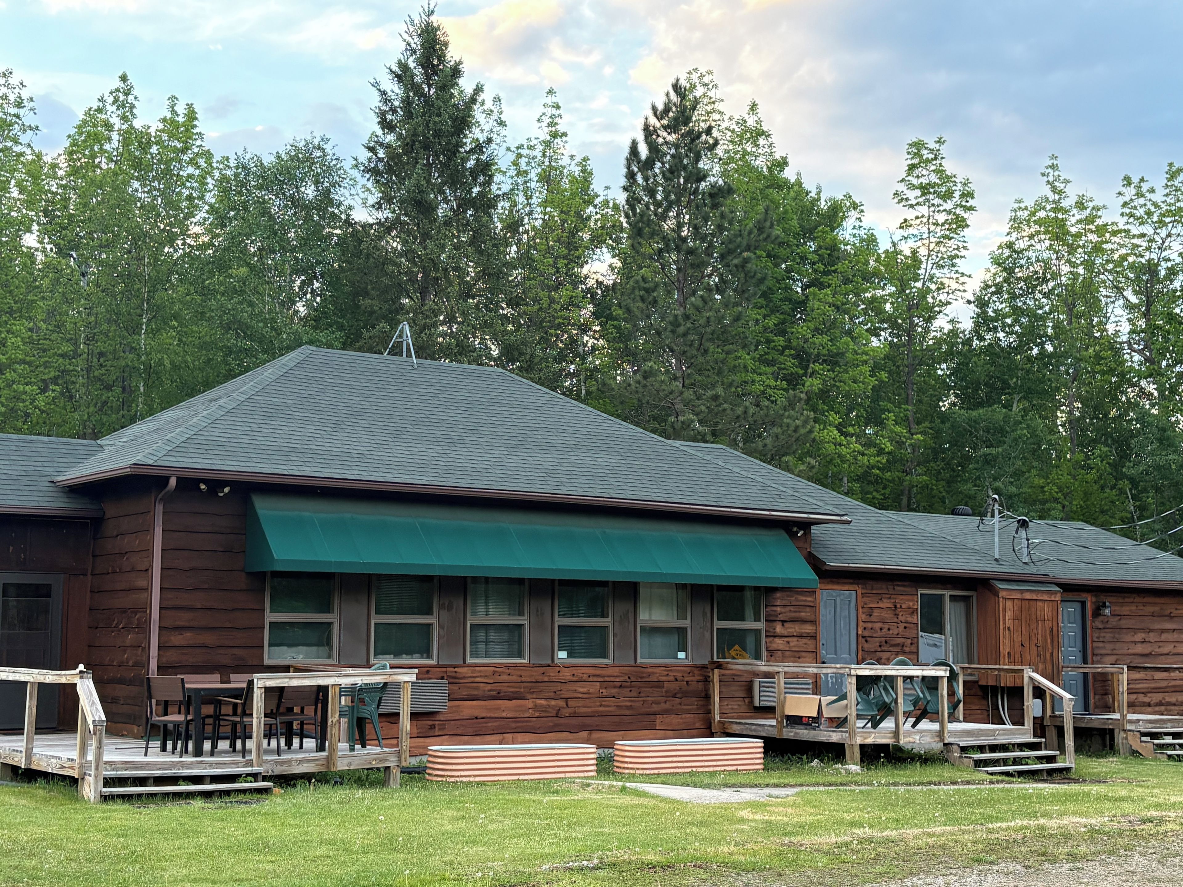 A wooden cabin with a green awning, a deck, and a staircase leading to the entrance.