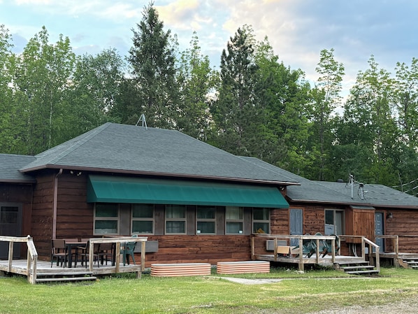A wooden cabin with a green awning, a deck, and a staircase leading to the entrance.