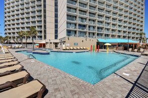 Área de piscina de hotel com vários níveis de varandas, espreguiçadeiras e uma piscina azul cristalina.