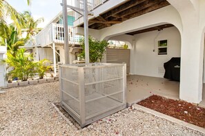A covered outdoor area with a grill, a metal fence, and a gravel ground. - Hooked on Little Torch: 3BR Escape with 40' Dock, 15,000 lb Boat Lift & Elevator (Little Torch Key)
