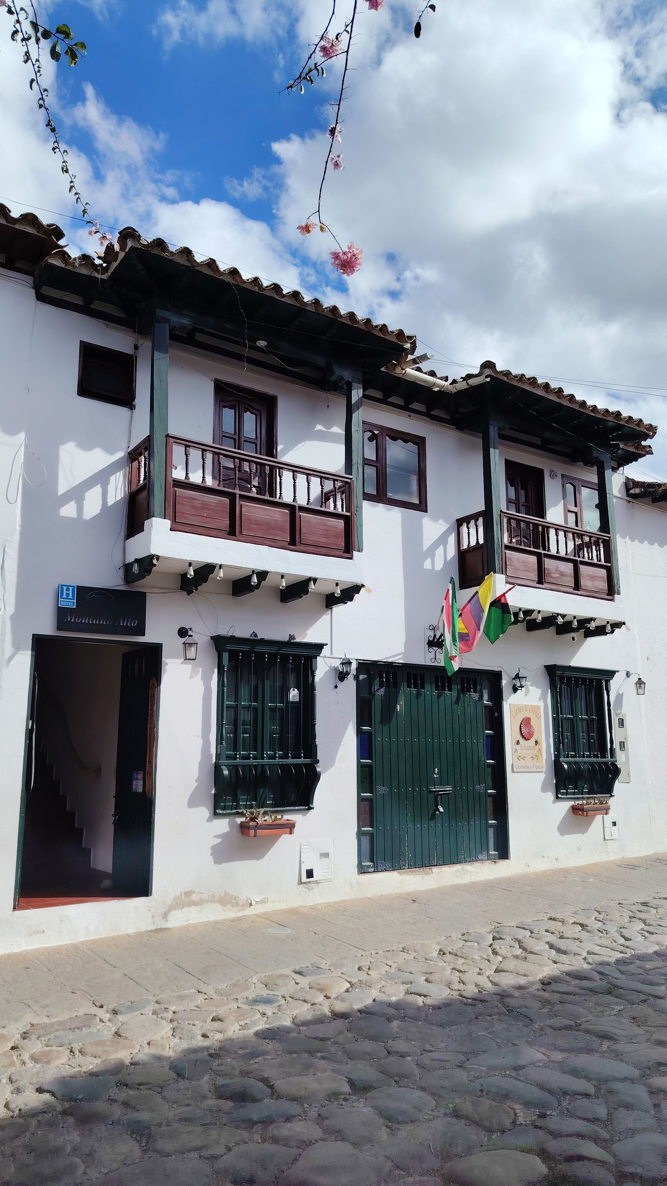 A two-story building with a balcony, a sign indicating a hotel, and a green gate.