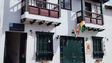A two-story building with a balcony, a sign indicating a hotel, and a green gate.