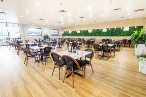 A spacious dining area with multiple tables and chairs, a green wall with plants, and a large window providing natural light. - Coco Key Hotel 2 Double Studio Water Park Arcade (Orlando)