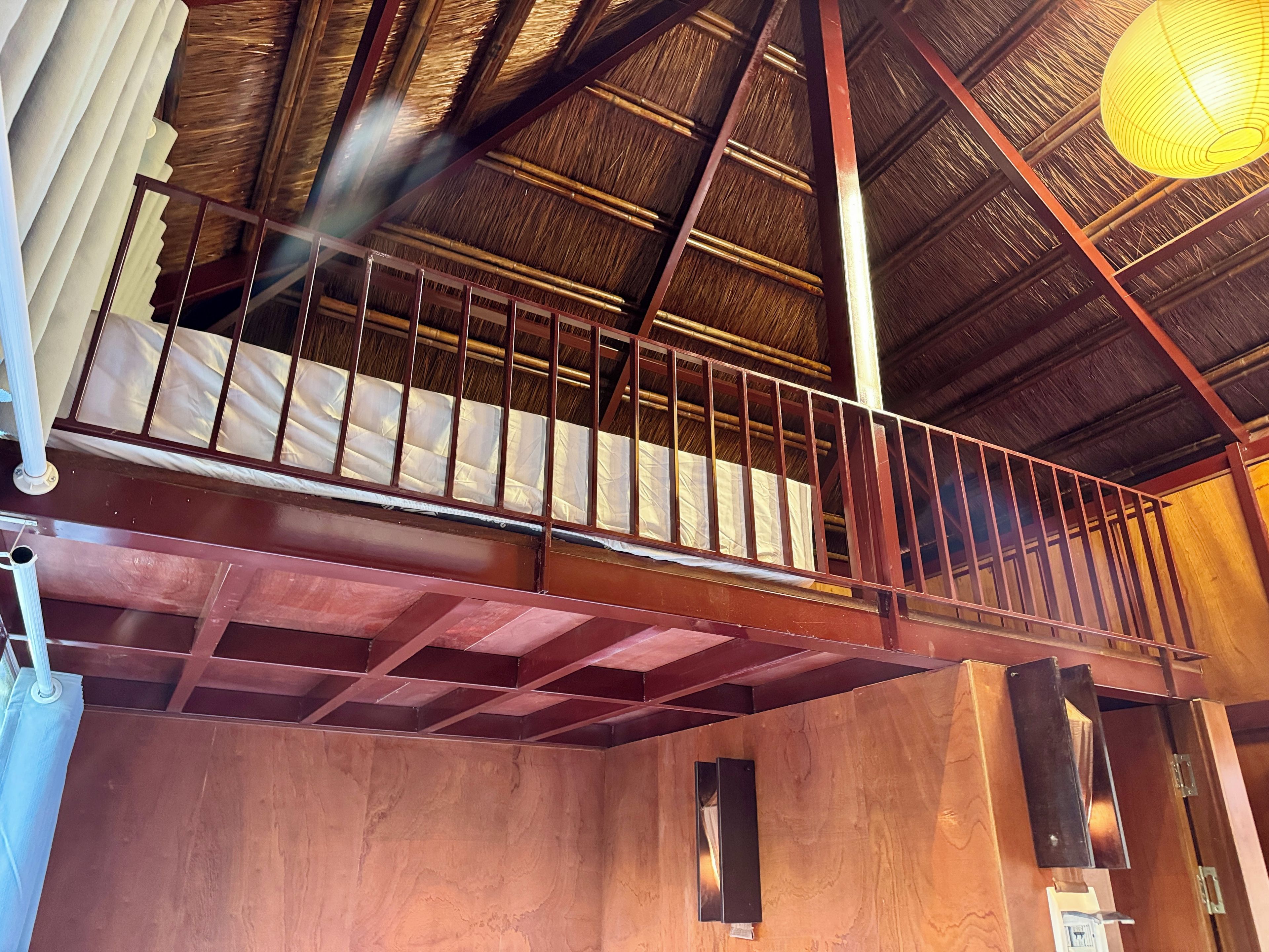 A wooden balcony with metal railings, a thatched roof, and a hanging light fixture.