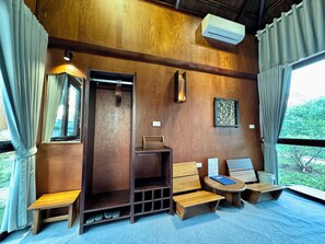 A room with a wooden ceiling, a built-in wardrobe, a small seating area with a bench and a table, and a window with curtains.
