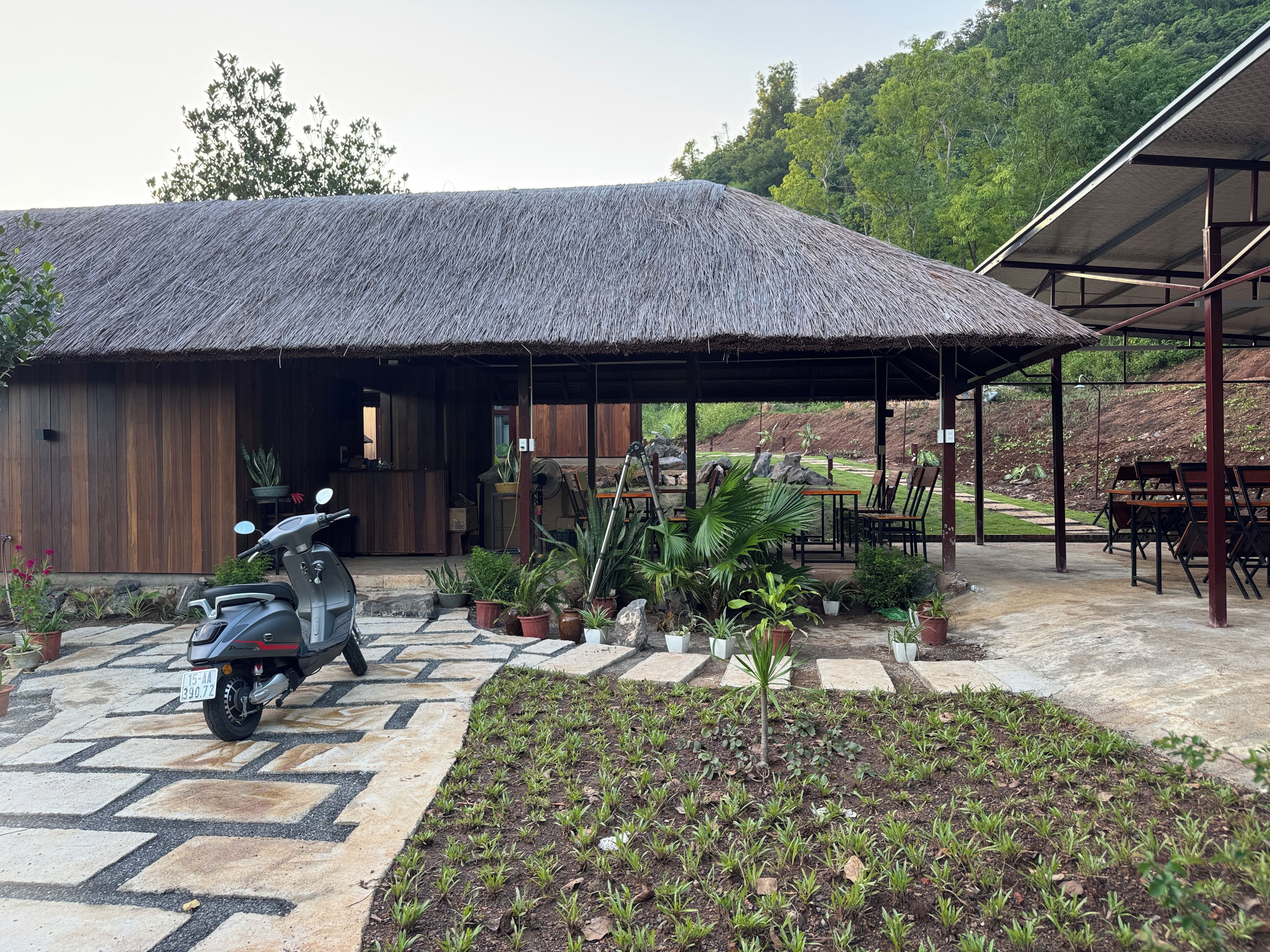 A thatched-roof building with a paved entrance and a scooter parked outside.