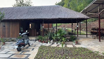 A thatched-roof building with a paved entrance and a scooter parked outside.