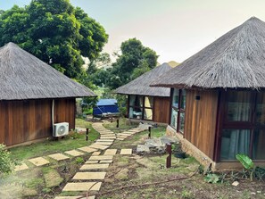 A pathway leading to thatched-roof huts with wooden walls, surrounded by greenery.