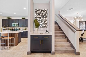 A modern kitchen with dark cabinetry, a central island, and a decorative wall piece. - Experience Magic and Luxury Just Minutes from Disney (Florida)