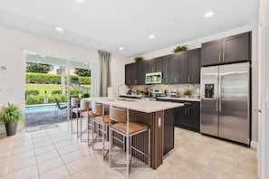 A modern kitchen with a central island, dark cabinetry, stainless steel appliances, and a view of a swimming pool. - Experience Magic and Luxury Just Minutes from Disney (Florida)