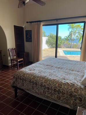 A bedroom with a bed, a chair, a desk, a ceiling fan, and a view of a swimming pool and palm trees. - Wonderful 2-bedroom house with AC in San José del Cabo (San José del Cabo)