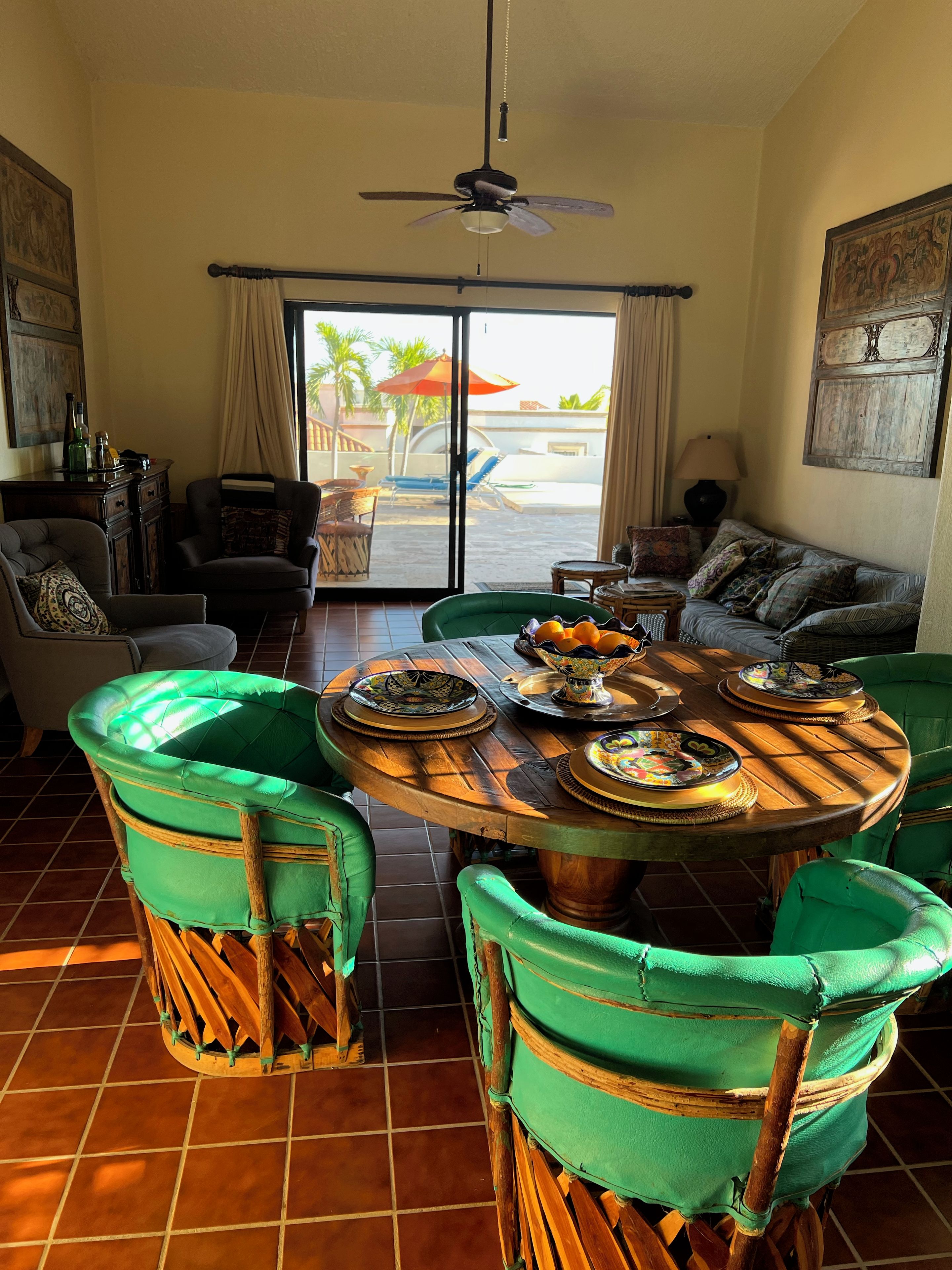 A dining area with a round table, green upholstered chairs, and a view of the outdoors through a glass door.