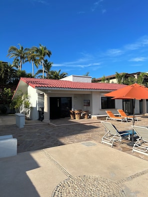 A building with a red-tiled roof, outdoor seating area with chairs and tables, and palm trees in the background. - Wonderful 2-bedroom house with AC in San José del Cabo (San José del Cabo)
