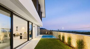 Een modern huis met een zwembad, een glazen patio en uitzicht op zee.