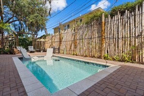 A swimming pool with a bamboo fence, lounge chairs, and a brick patio. - Carriage House in the trees, Historic St. Augustine (St. Augustine)