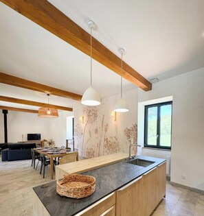 A modern kitchen with wooden beams, pendant lights, and a large island. - Gîtes de France® - La Maison du Ratier (LES ARQUES)