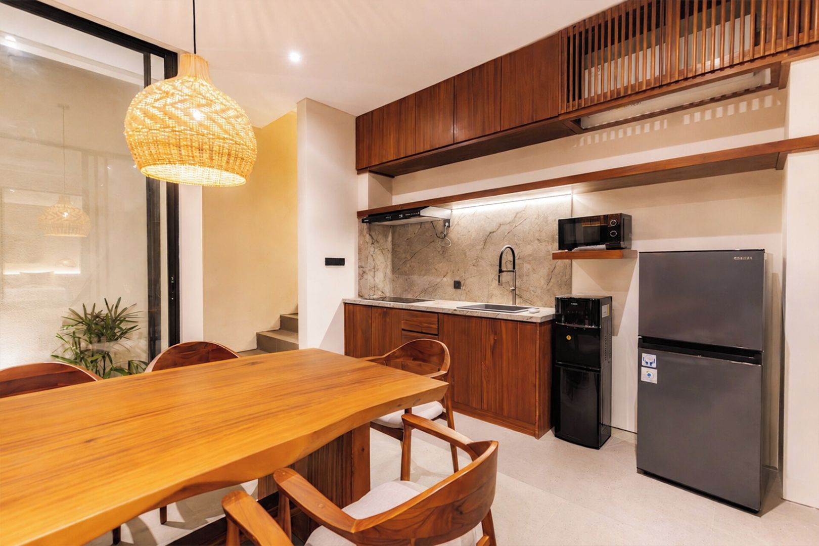 Een moderne keuken met houten kastjes, een marmeren aanrecht, een ingebouwde oven en een eetgedeelte met een houten tafel en stoelen.