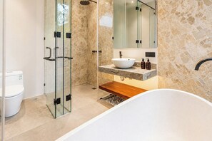 Un baño moderno con ducha de vidrio, bañera independiente y tocador con azulejos de mármol.