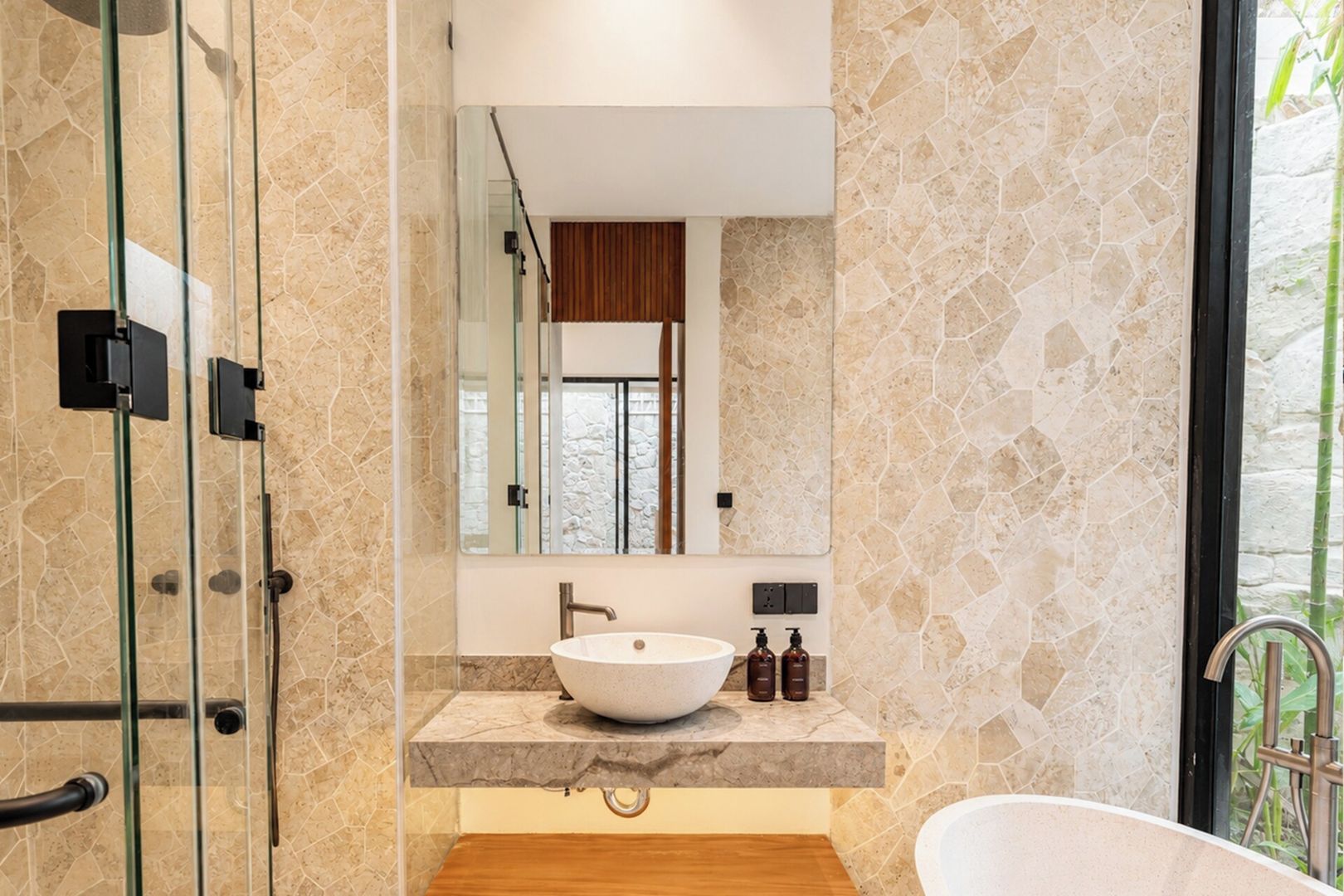Une salle de bain moderne dotée d’une douche à parois de verre, d’une baignoire sur pieds et d’un grand miroir au-dessus d’un plan de toilette en marbre.