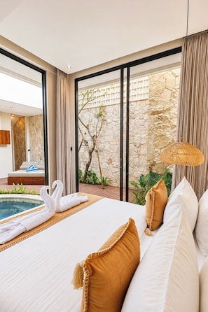 Een hotelkamer met een groot bed, uitzicht op een zwembad en een stenen muur.