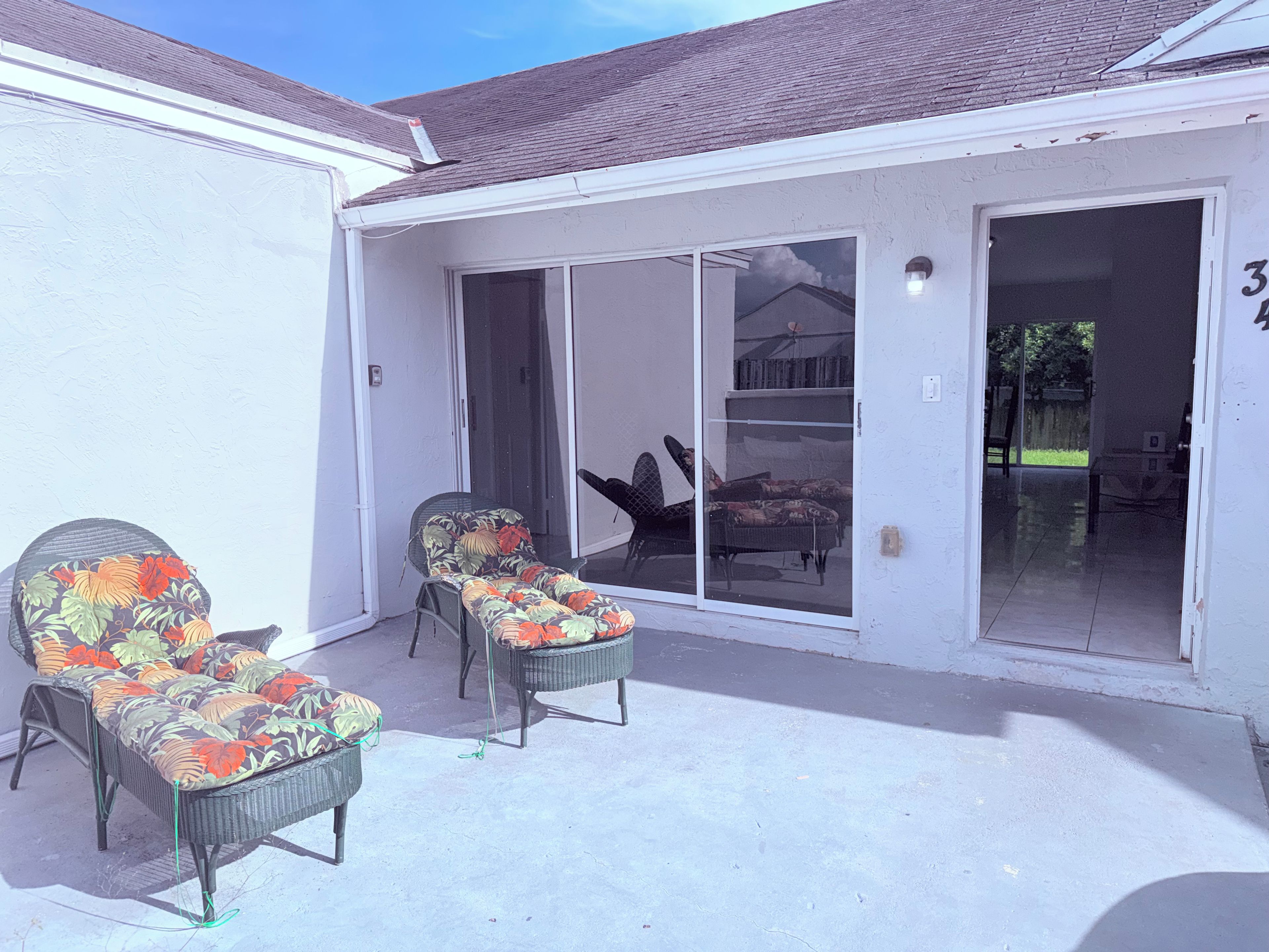 A covered patio with two wicker chairs and a sliding glass door leading to an indoor area.