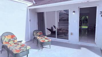 A covered patio with two wicker chairs and a sliding glass door leading to an indoor area.