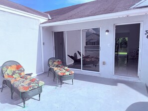A covered patio with two wicker chairs and a sliding glass door leading to an indoor area.