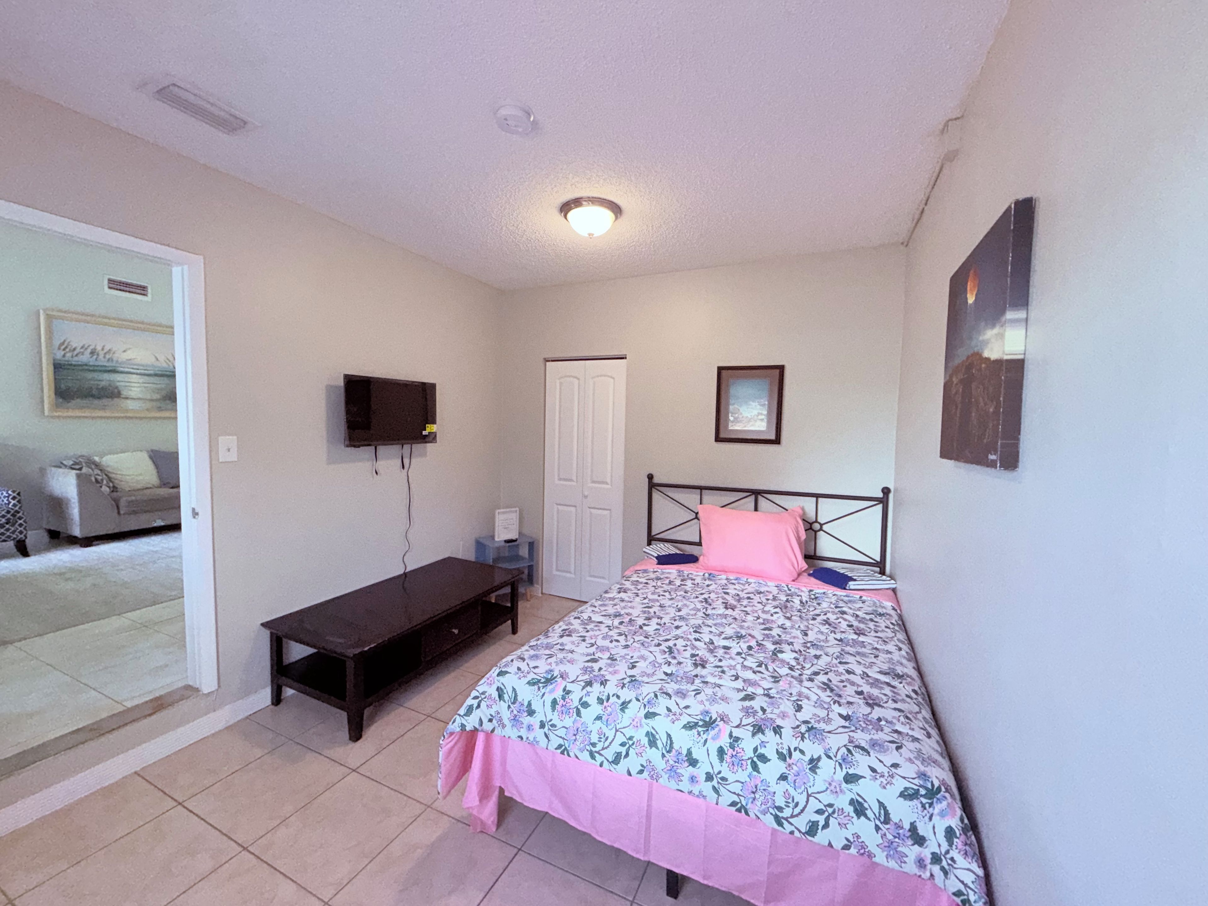 A bedroom with a bed, a television mounted on the wall, a door, and a small table.