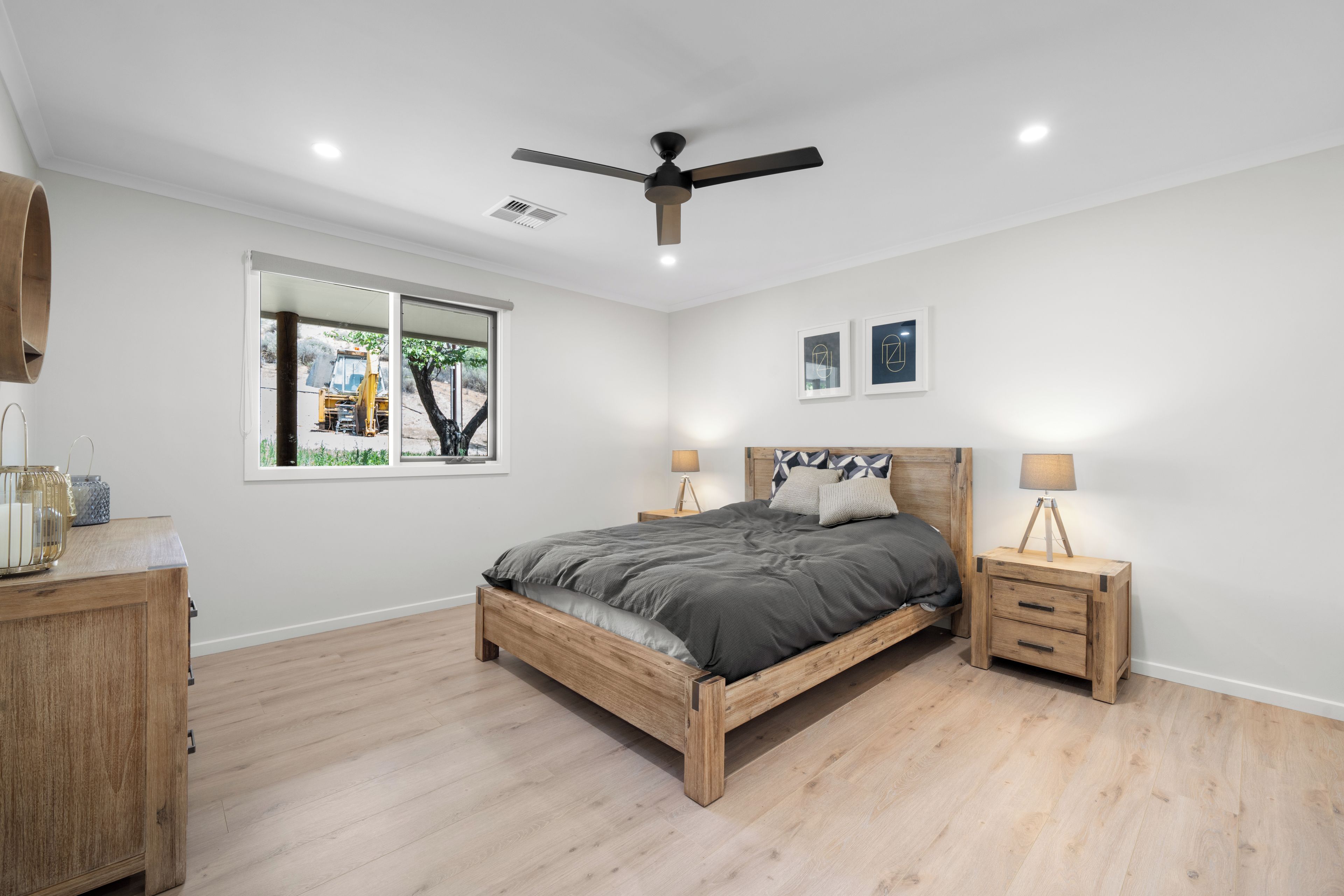 A bedroom with a wooden bed, nightstands, a ceiling fan, a window with a view, and two framed pictures on the wall.