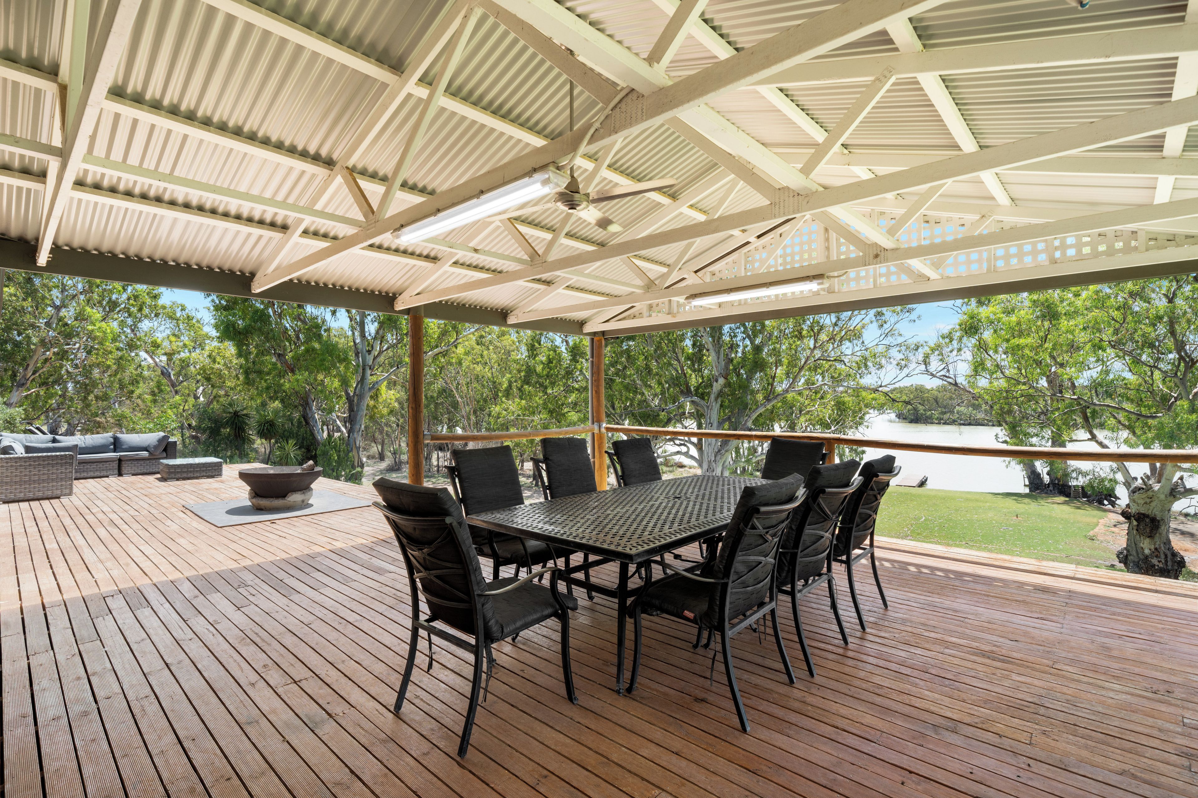 An outdoor patio with a table and chairs, surrounded by wooden decking and a view of trees and water.
