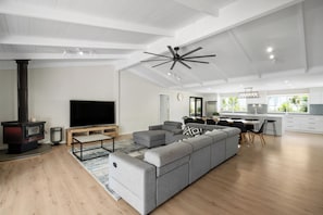 A modern living room with a large gray sectional sofa, a flat-screen TV, and a wood-burning stove.