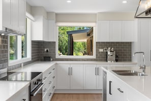 A modern kitchen with white cabinetry, a built-in oven, and a window with a view of greenery.