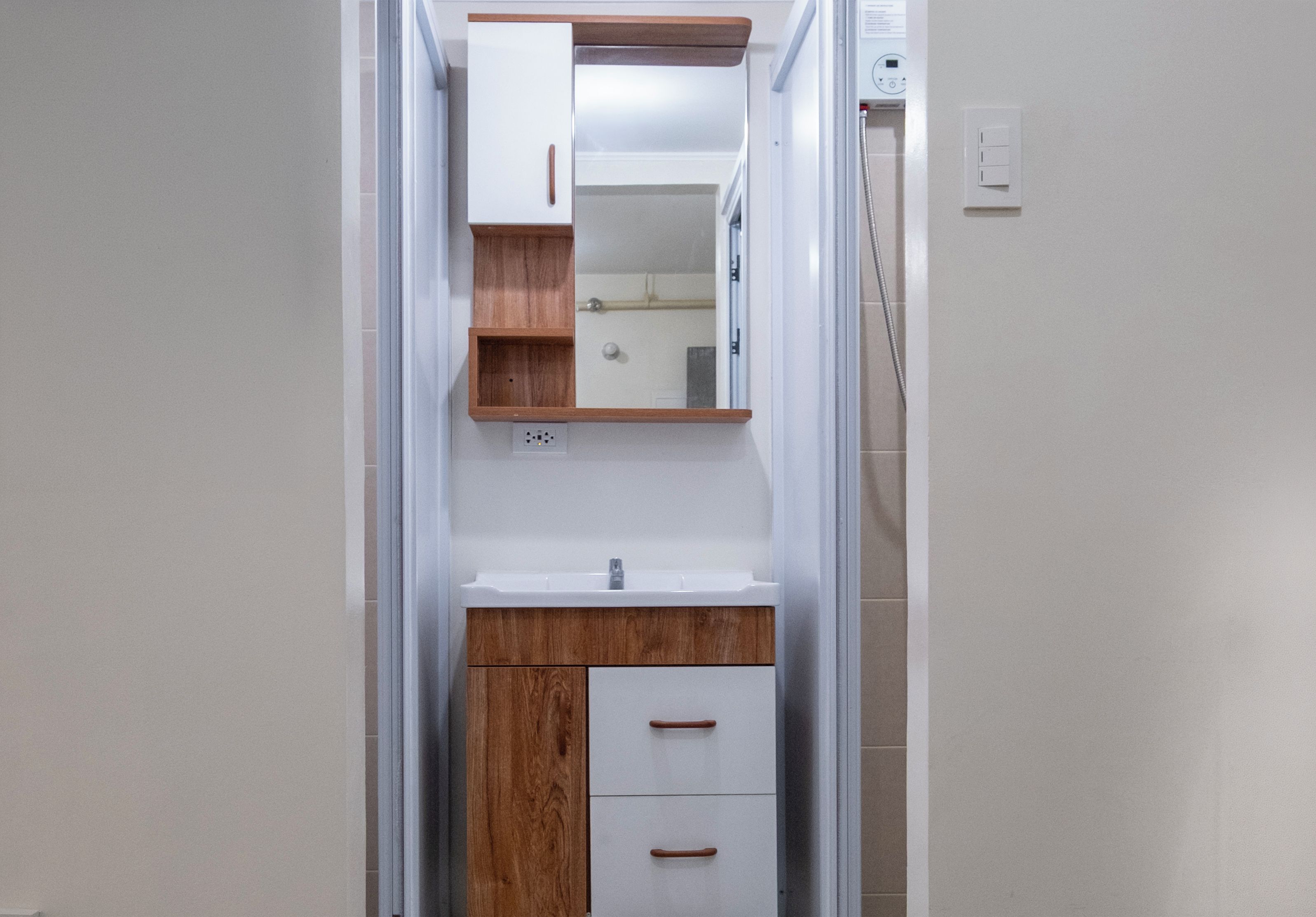 Un baño estrecho con tocador de madera, espejo y lavamanos blanco.