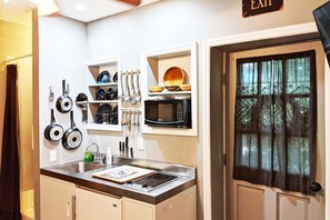 A kitchen with a built-in microwave, a sink, and a stove. There are utensils hanging on the wall and a door with a curtain. - Courtyard Studio, Short walk to Historic District (St. Augustine)