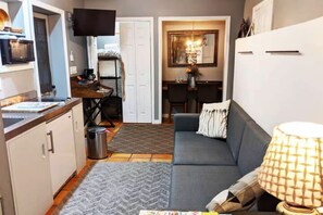 Ett kompakt bostadsutrymme med ett litet kök, en soffa, ett matbord och en TV som är monterad på väggen.