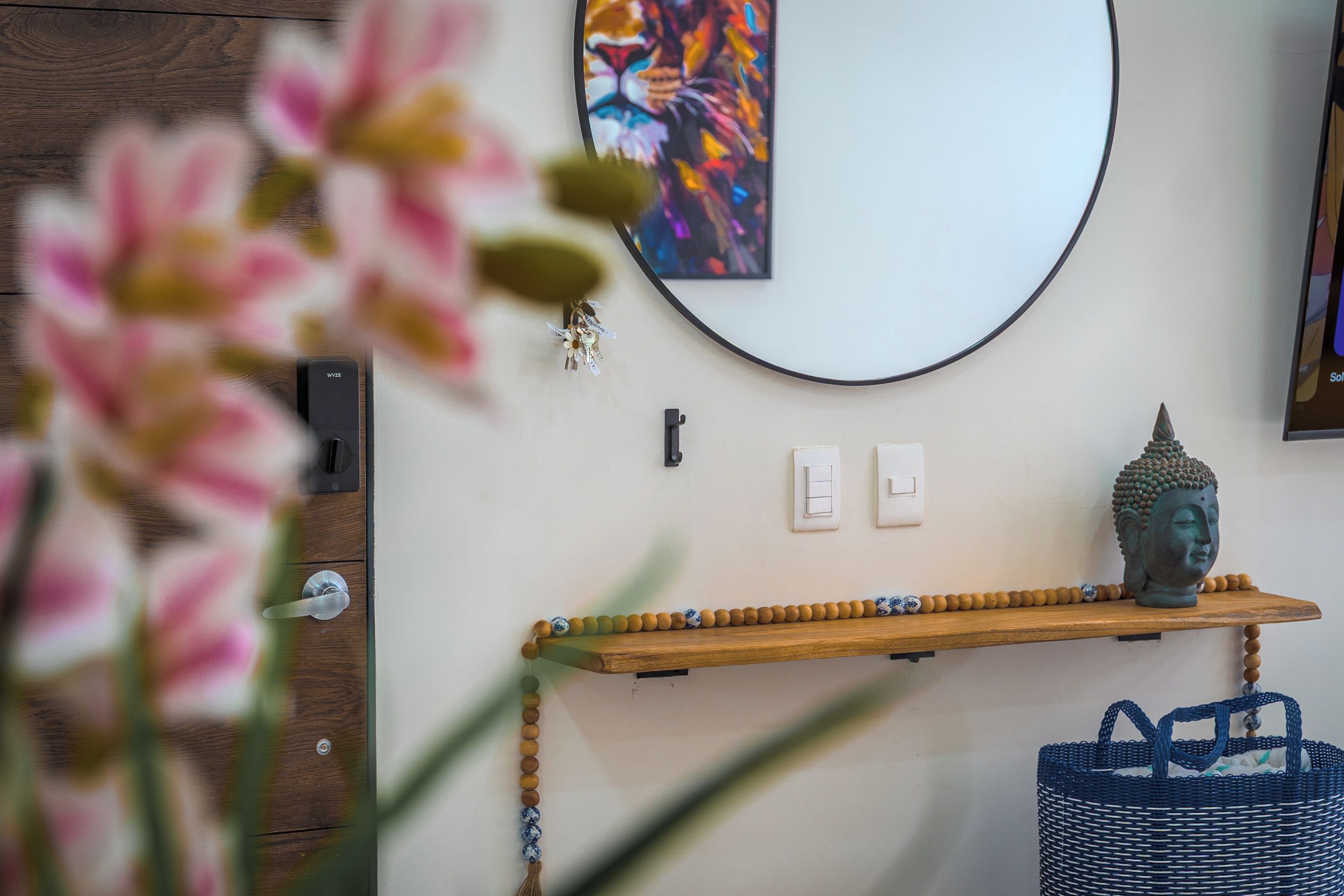 A room with a wooden shelf holding a Buddha statue, a wall-mounted light switch, and a colorful abstract painting.