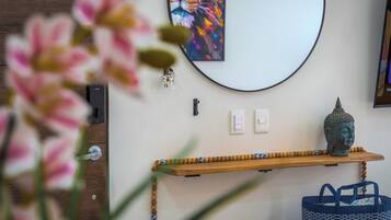 A room with a wooden shelf holding a Buddha statue, a wall-mounted light switch, and a colorful abstract painting.