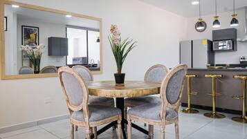 Een eetruimte met een ronde houten tafel, vier gestoffeerde stoelen, een potplant en een grote spiegel aan de muur.