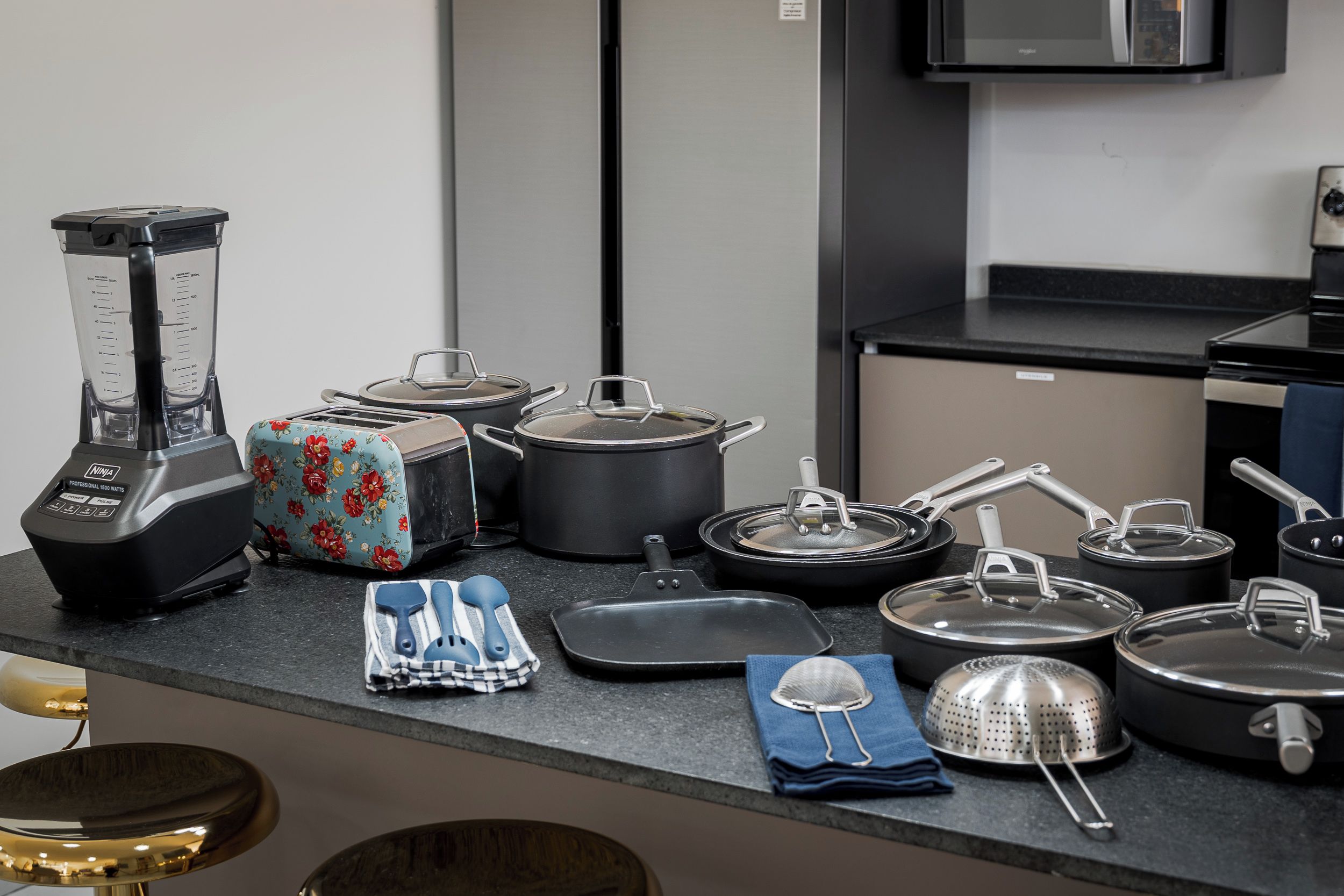 A kitchen with a blender, toaster, pots, pans, and a strainer on the counter.