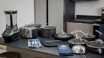 A kitchen with a blender, toaster, pots, pans, and a strainer on the counter.