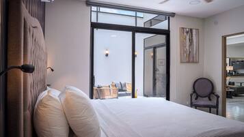 A modern bedroom with a large bed, a view through a glass door, a chair, and a painting on the wall.