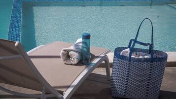 A poolside area with a lounge chair, a towel, a water bottle, and a woven bag.